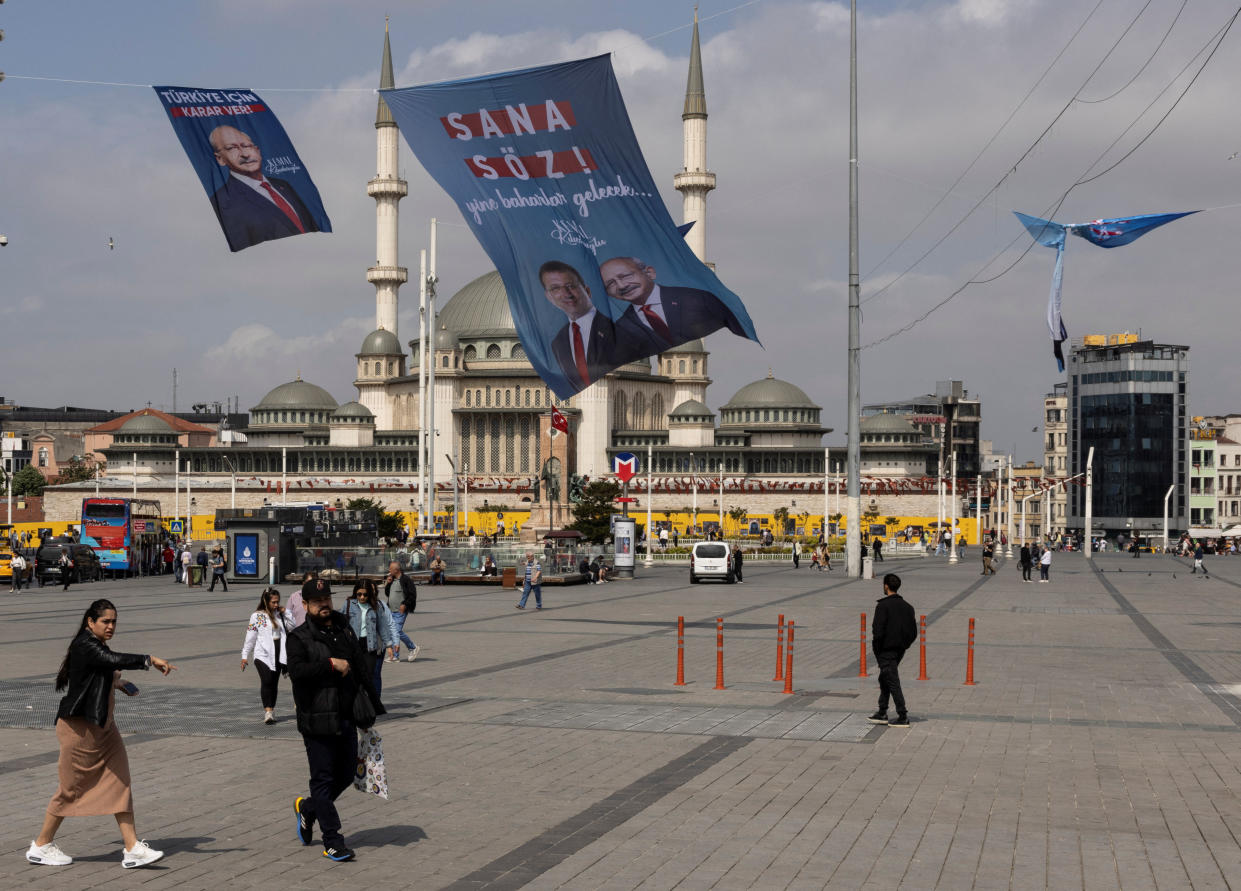 With the minarets of a mosque in the background, people cross a huge empty plaza.