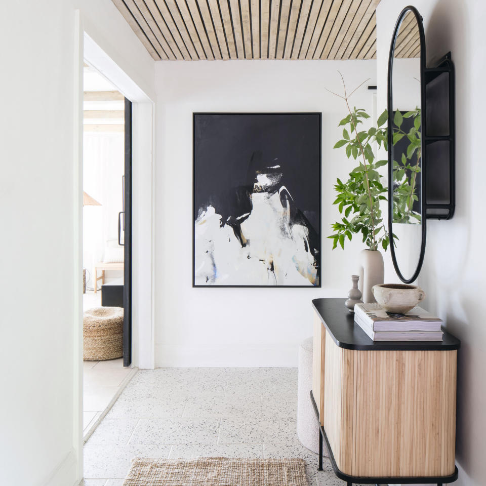 Wide white painted hallway with black and natural wood console table furnished with home decor, hanging mirror, and hanging artwork