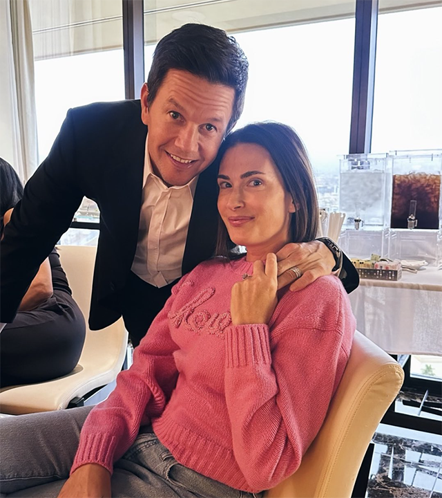 Mark Wahlberg in a black suit puts his arm around Rhea Durham sitting in a pink sweater