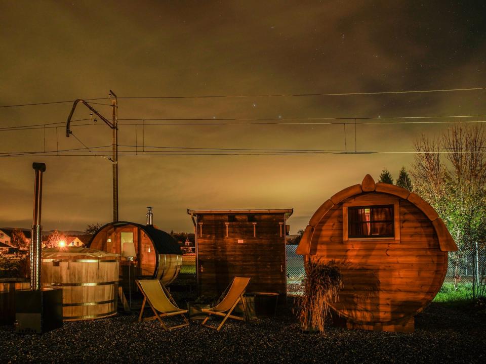 A cyclindrical tiny home next to another small building with two deck chairs in front of it, at night.