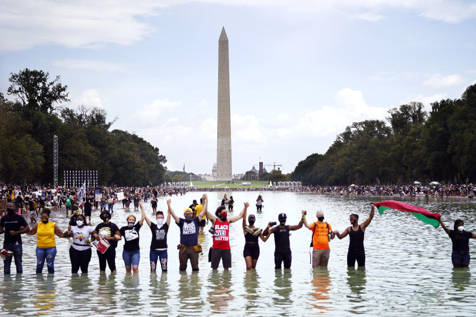 People pose for a group photo in the Reflecting Pool in the shadow of the Washington Monument as they attend the March on Washington, Friday, Aug. 28, 2020, at the Lincoln Memorial in Washington, on the 57th anniversary of the Rev. Martin Luther King Jr.'s "I Have A Dream" speech. (AP Photo/Julio Cortez)