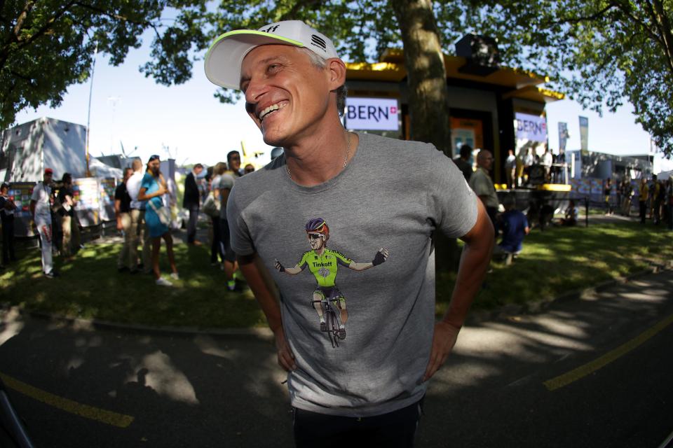 A man in a bike t-shirt poses in front of a tree where people are gathered.