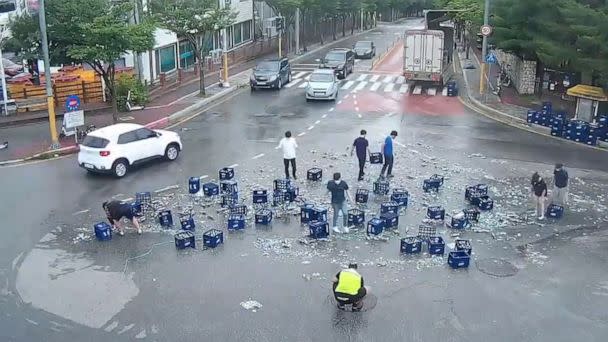 PHOTO: People help clean up bottles of beer that fell off a truck as the driver made a sharp turn in Chuncheon, South Korea, June 29, 2022. (KBS)