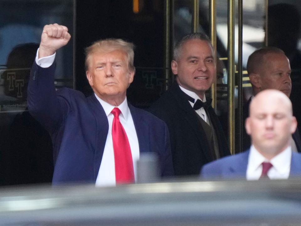 Donald Trump holds up a fist to onlookers as he leaves to be taken into custody and arraigned.