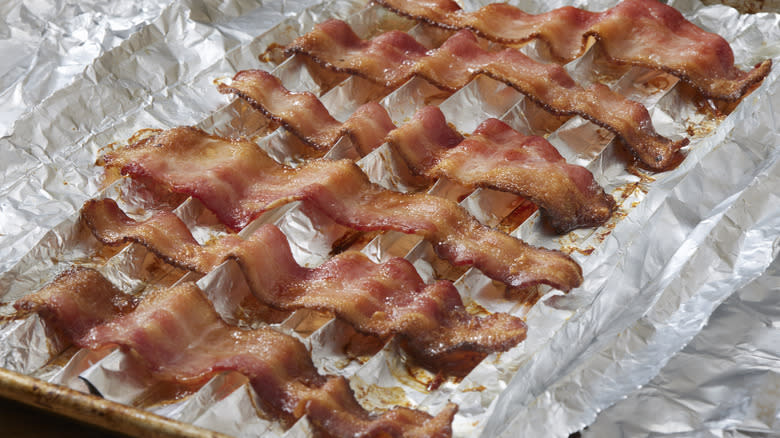 strips of bacon cooking on aluminum-lined sheet