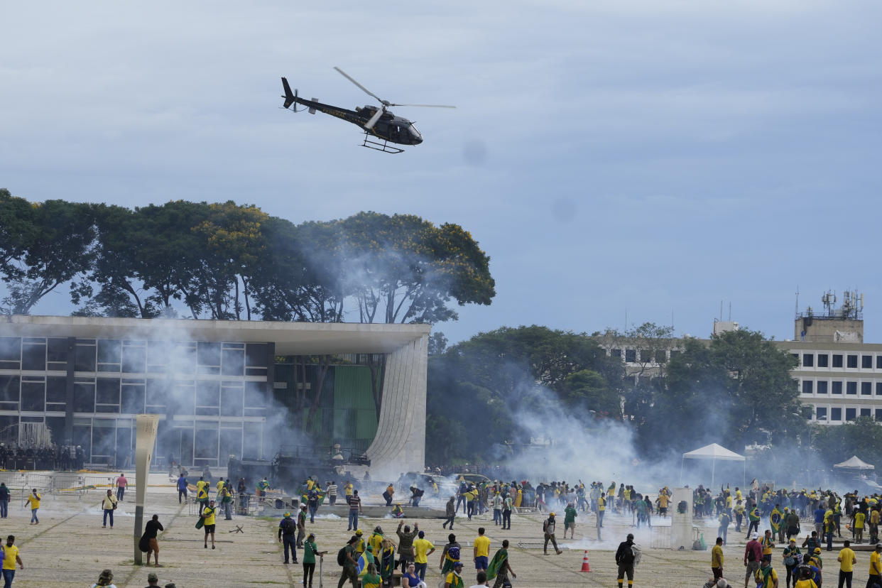 A helicopter hovers above supporters of Brazil's former President Jair Bolsonaro and clouds of what may be tear gas rise over the plaza.