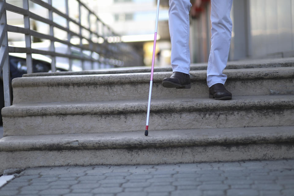 Close up of a young man with white support cane walking down the stairs.