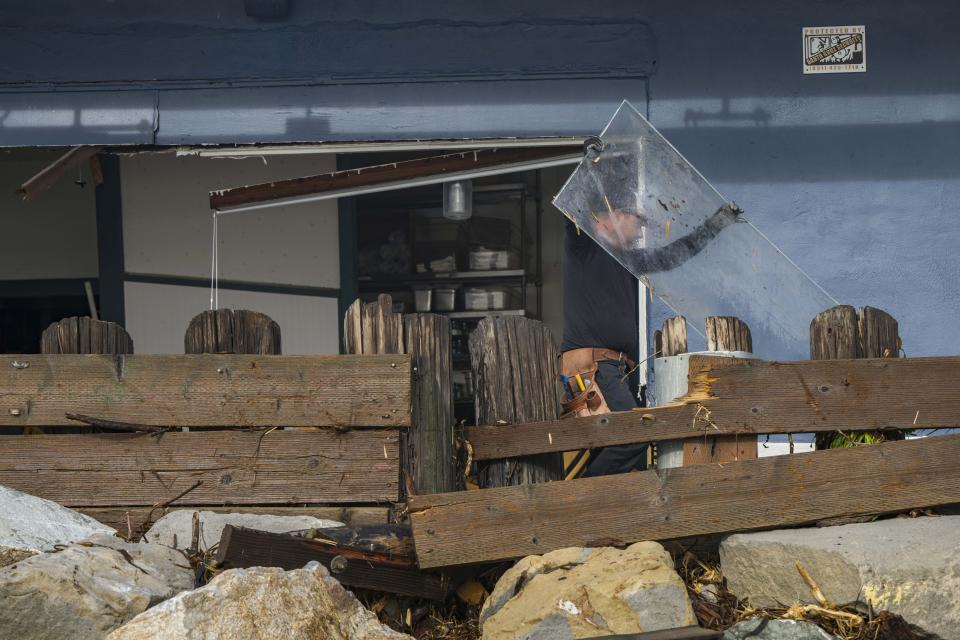 A man removes debris from Zelda's on the Beach after the restaurant was damaged in a storm in Captiola, Calif., Thursday, Jan. 5, 2023. Damaging hurricane-force winds, surging surf and heavy rains from a powerful “atmospheric river” pounded California on Thursday, knocking out power to tens of thousands, causing flooding, and contributing to the deaths of at least two people, including a child whose home was hit by a falling tree. (AP Photo/Nic Coury)