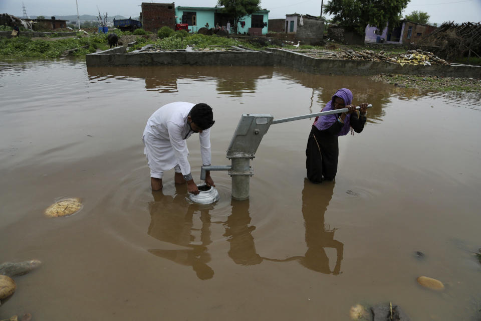 Indios recogen agua potable de una bomba manual en una calle anegada por las lluvias del monzón en Jammu, India, el 13 de agosto de 2018. (AP Foto/Channi Anand)