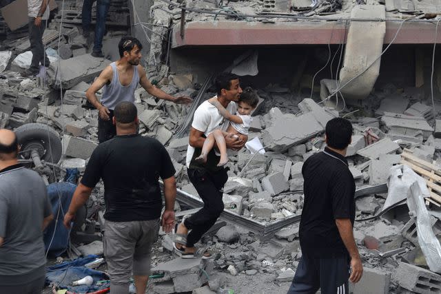 <p>EYAD AL-BABA/AFP via Getty </p> A Palestinian man carries a child rescued from the Tattari family home which was destroyed in an Israeli airstrike on Gaza City