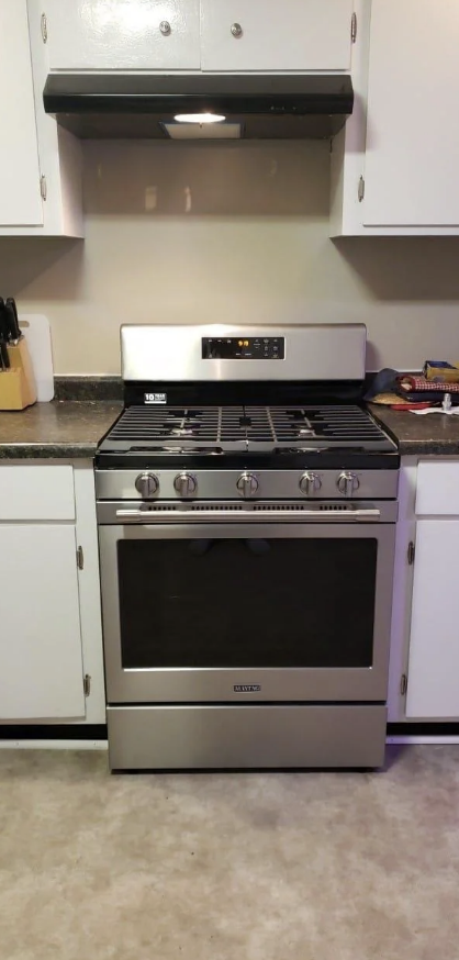 A stainless steel gas range oven is placed in the center of the white kitchen cabinets with a range hood above it.