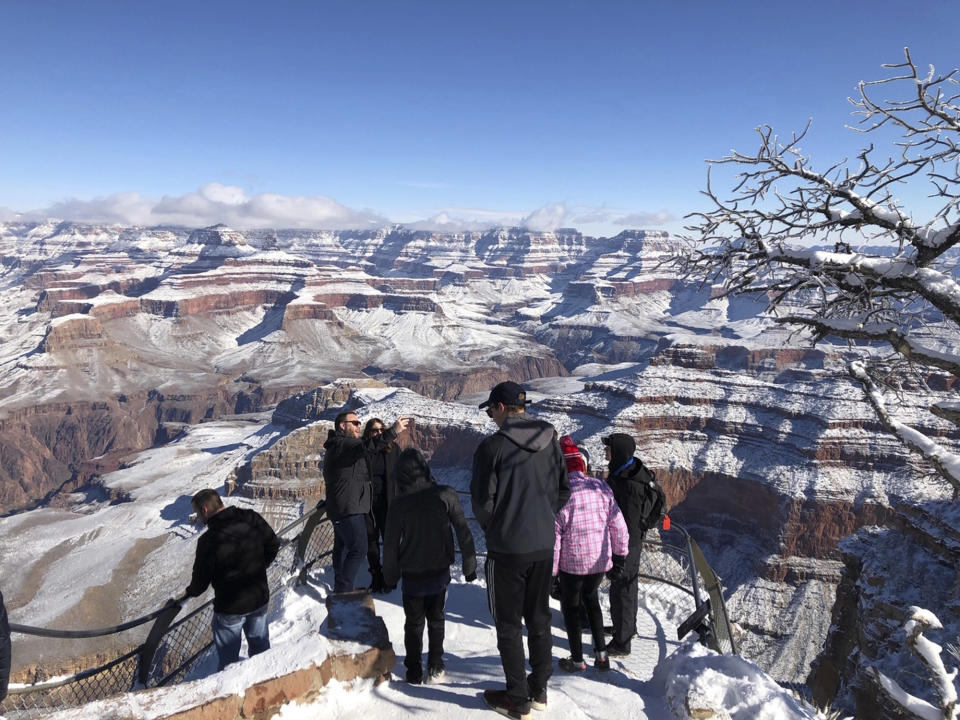 In this Tuesday, Jan. 1, 2019, photo, tourists look at and take photos of a snow-covered Grand Canyon, in Arizona. A winter storm has covered cactus with snow in parts of the American Southwest as temperatures in the desert fall below those of Anchorage, Alaska. (AP Photo/Anna Johnson)
