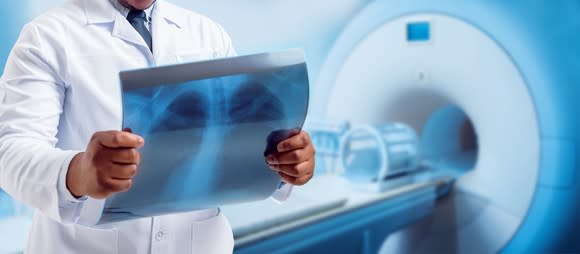 A doctor is reading a medical scan film in front of an MRI machine.