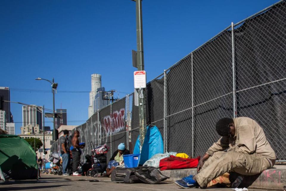 Homeless people sit on the sidewalk by the non-profit Midnight Mission’s headquarters, while traditional Thanksgiving meals are served to nearly 2000 homeless people in the Skid Row neighborhood of downtown Los Angeles on November 25, 2021. (Photo by Apu GOMES / AFP) (Photo by APU GOMES/AFP via Getty Images)