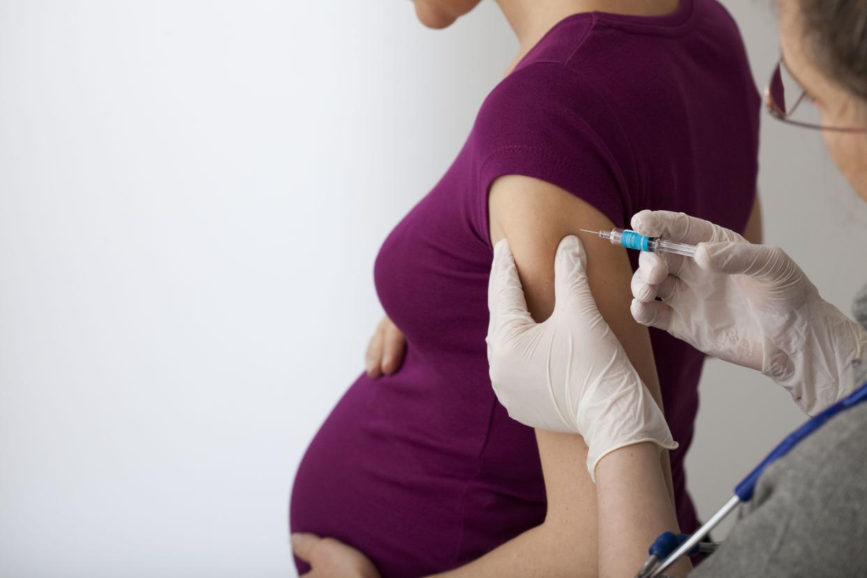 pregnant woman getting vaccine in arm from doctor wearing gloves