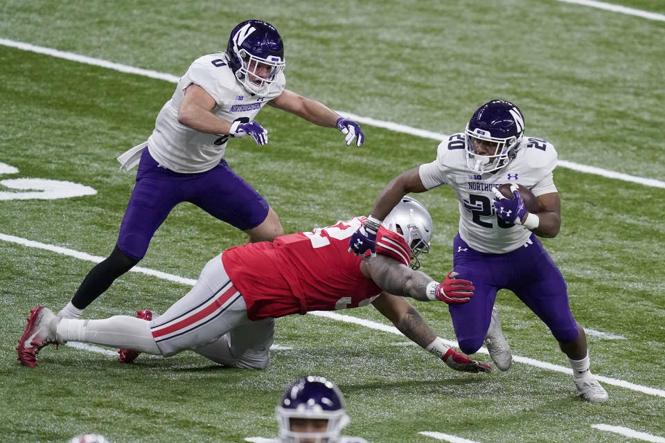 Northwestern running back Cam Porter (20) runs with the ball as Ohio State defensive tackle Haskell Garrett defends and teammate John Raine (0) watches during the first half of the Big Ten championship NCAA college football game, Saturday, Dec. 19, 2020, in Indianapolis. (AP Photo/Darron Cummings)