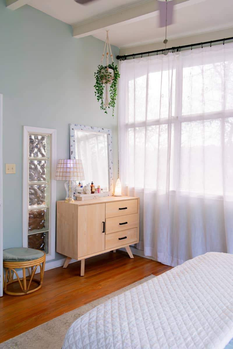 Bedroom with wooden floors,  light wooden dresser with lamp and fragrances.