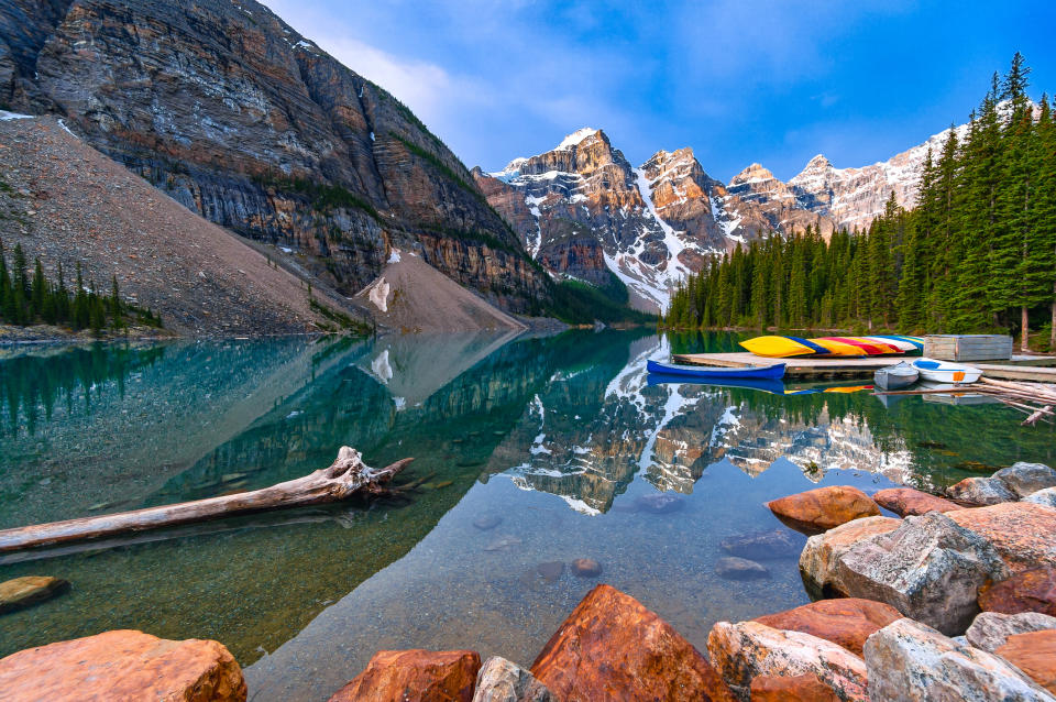 Mountain lake with kayaks by the shore and forested slopes reflecting in calm water