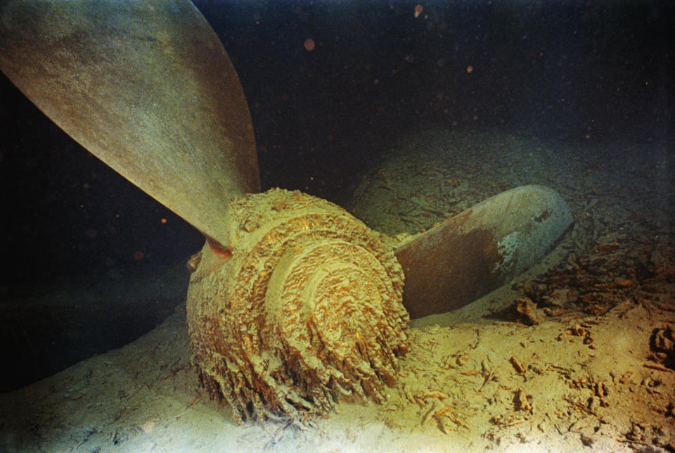 A rusty propeller from the wreckage of the RMS Titanic lies on the ocean floor, partially covered in sediment