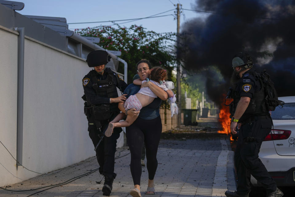 FILE - Israeli police officers evacuate a woman and a child from a site hit by a rocket fired from the Gaza Strip, in Ashkelon, southern Israel, Saturday, Oct. 7, 2023. Israel and Hamas have been at war for 100 days. The war already is the longest and deadliest between Israel and the Palestinians since Israel’s establishment in 1948, and the fighting shows no signs of ending. (AP Photo/Tsafrir Abayov, File)