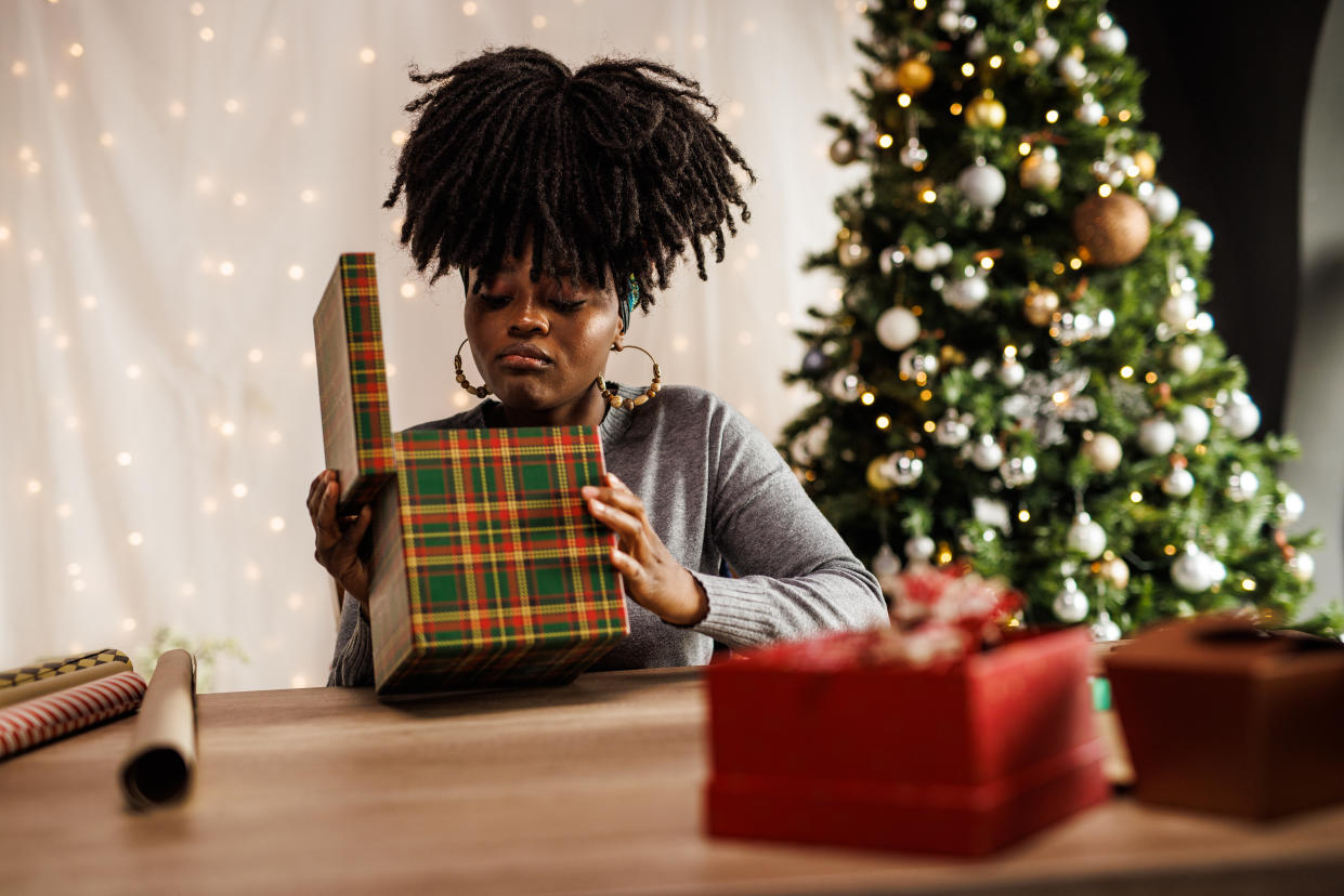 Portrait of disappointed young woman sitting at her home office desk and opening a Christmas icks gift box.