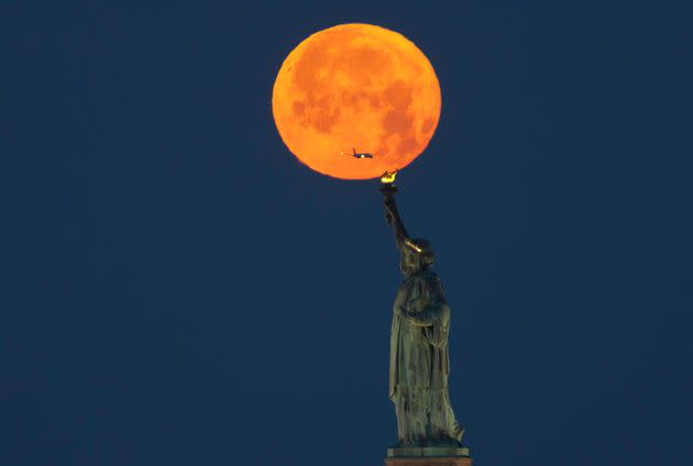 The full Strawberry Moon sets behind the Statue of Liberty before sunrise on June 4, 2023, in New York City.