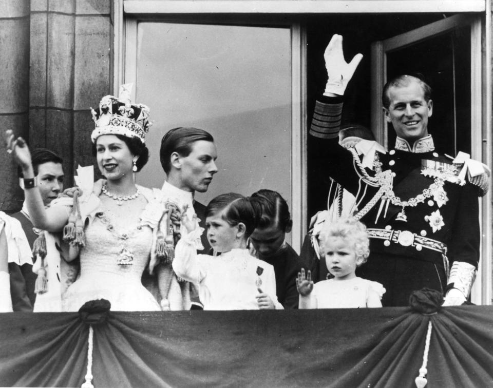 Queen Elizabeth II, Prince Philip, and their children, Prince Charles and Princess Anne, wave from the balcony at Buckingham Palace