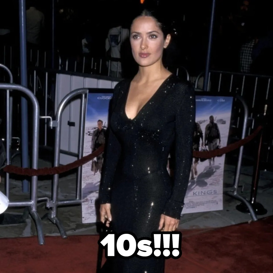 Salma Hayek on the red carpet wearing a long, elegant black dress with sequin details and holding a black purse