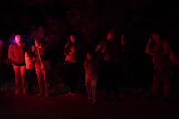 Onlookers are illuminated by police lights at the scene where officials say dozens of people have been found dead and multiple others were taken to hospitals with heat-related illnesses after a semitrailer containing suspected migrants was found, Monday, June 27, 2022, in San Antonio. (AP Photo/Eric Gay)