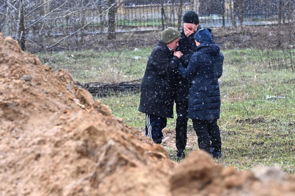 People react as they gather close to a mass grave in the town of Bucha, just northwest of the Ukrainian capital Kyiv on April 3, 2022.