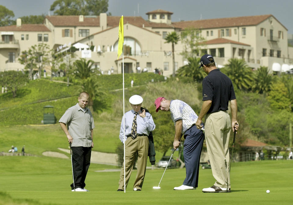 FILE - With the historic clubhouse in the background, Duffy Waldorf takes a practice putt at the 10th green as veteran teaching pro Eddie Merrins, in the tie, and golfer Arron Oberholser, right, watch during a practice session for the Nissan Open at Riviera Country Club, Feb. 18, 2003, in Los Angeles. Merrins died Wednesday, Nov. 22, 2023, at age 91. (AP Photo/Reed Saxon, File)