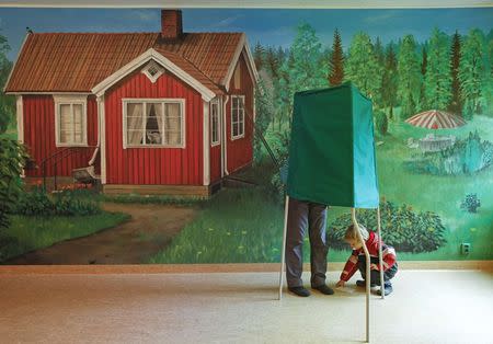 A man and a boy stand at a booth in front of a mural at a polling station during general elections in Stockholm in this September 19, 2010 file photo. REUTERS/Soren Andersson/TT News Agency/Files