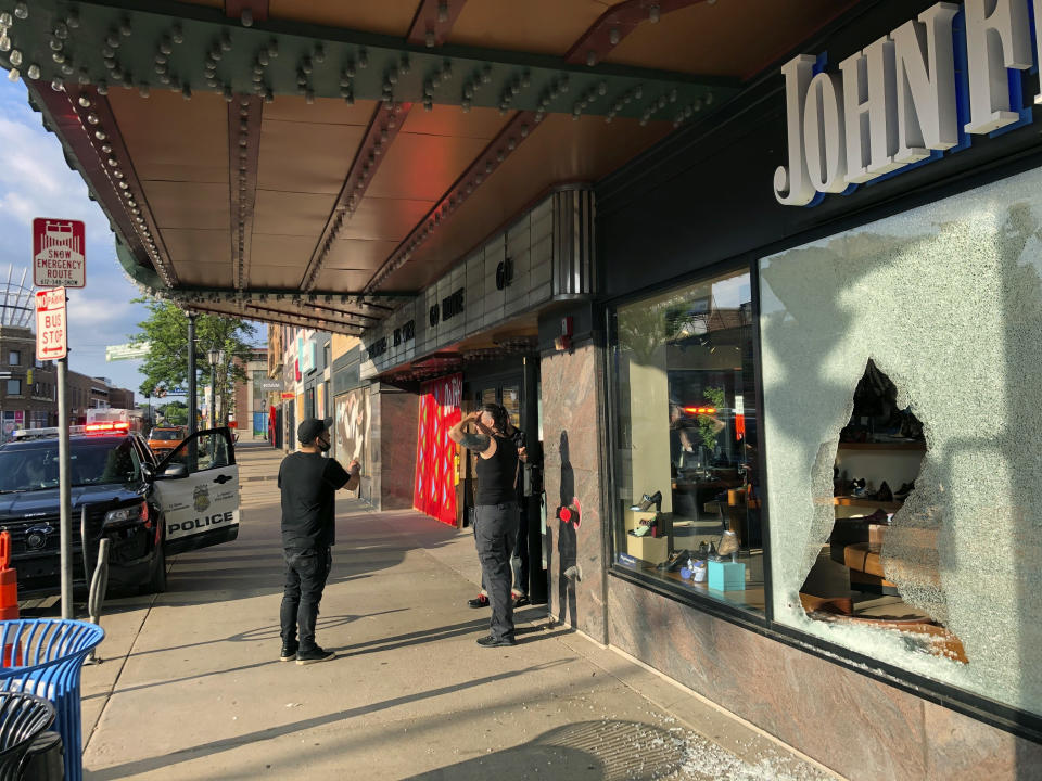People stand near a storefront of a shoe store damaged by gunfire as a police vehicle remains on the scene outside the Uptown Theatre Sunday, June 21, 2020, following a shooting in Minneapolis' Uptown neighborhood. Multiple people were shot, one fatally, when gunfire broke out shortly after midnight Sunday. (AP Photo/Doug Glass)