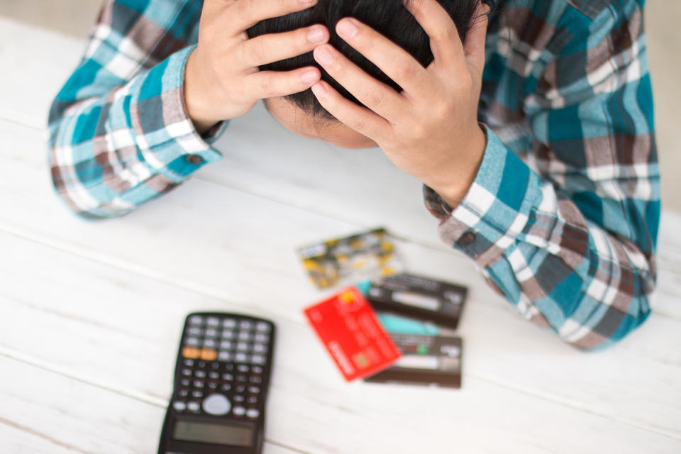 Person in financial difficulty holds their head in their hands with credit cards and a calculator on the desk.