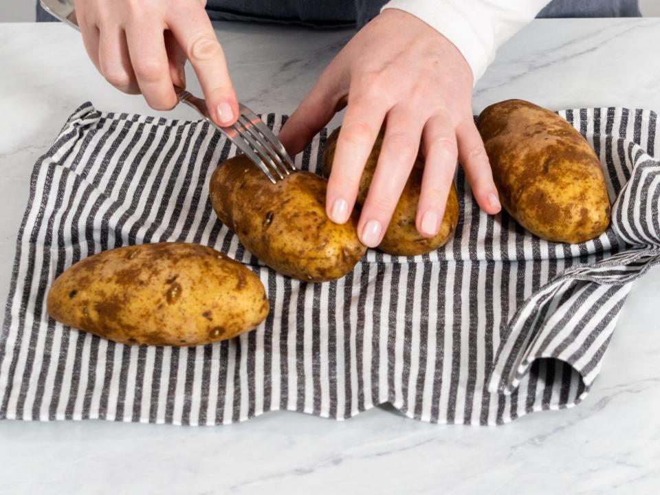 person poking potatoes with a fork as they rest on a stripped kitchen towel on a counter