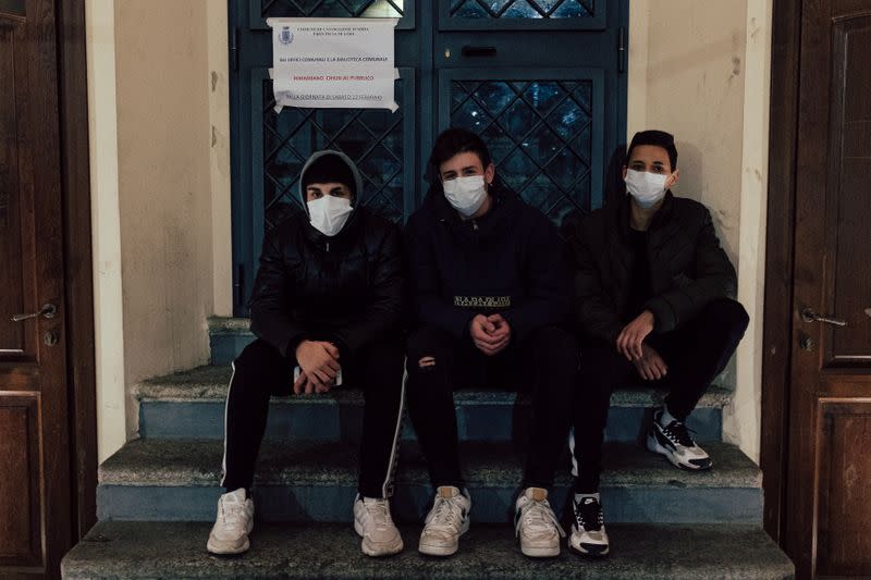 Three boys wearing protective face masks sit outside a closed public building in San Fiorano, one of the towns on lockdown due to a coronavirus outbreak, in this picture taken by 35-year-old schoolteacher Marzio Toniolo in San Fiorano