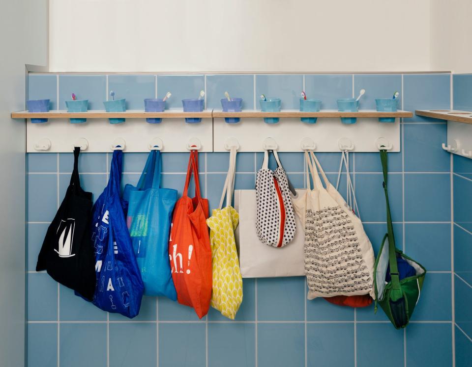 Colorful tote bags hanging on hooks with cups with one toothbrush above each in a German preschool