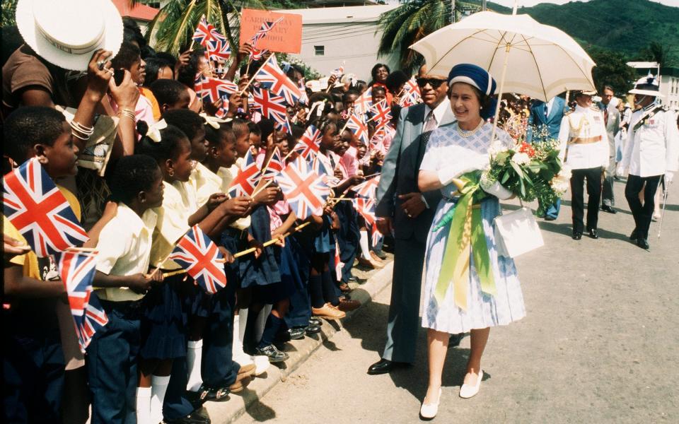 Queen Elizabeth II walks with an umbrella to shield herself from the sun during a state visit to the British Virgin Islands in 1977. - Anwar Hussein/Getty Images