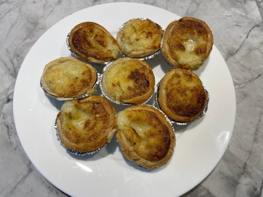 Eight golden-brown Portuguese custard tarts on a white plate on a gray counter
