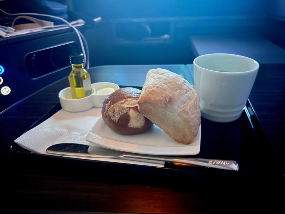 Two bread rolls on a plate with butter and oil on the side next to a butter knife.