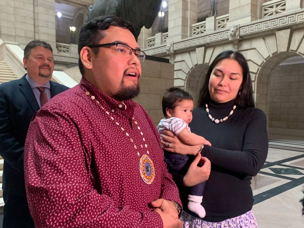 Zaagaate Jock holds her newborn, Atetsenhtsén:we, while her partner, Carson Robinson, speaks to the media about their push to get Manitoba to formally recognize their daughter's name. NDP MLA Ian Bushie, background, introduced a bill in order to amend the Vital Statistics Act to recognize these names. (Ian Froese/CBC - image credit)