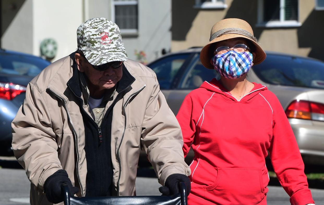 A woman wears a face mask as an elderly couple walk on a street in Alhambra, California on February 4, 2020. - As the coronavirus outbreak  spreads, fueling rumors and misinformation, a petition to cancel all classes in one US school district for fear of the virus has garnered nearly 14,000 signatures. The online petition posted on Change.org urges the Alhambra Unified School District located east of Los Angeles and with a heavily Asian population, to basically shut down until the outbreak is over. School district officials, however, have dismissed the petition as a bid to whip up hysteria over the deadly outbreak that has killed hundreds in China. (Photo by Frederic J. BROWN / AFP) (Photo by FREDERIC J. BROWN/AFP via Getty Images)
