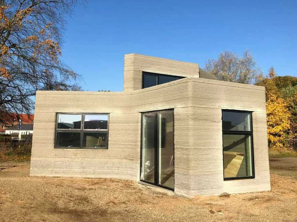 The 3D printed home among trees and a blue sky.