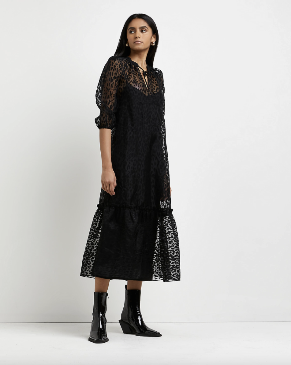 model with black hair and black boots in black River Island Tie Neck Midi Dress (Photo via River Island)