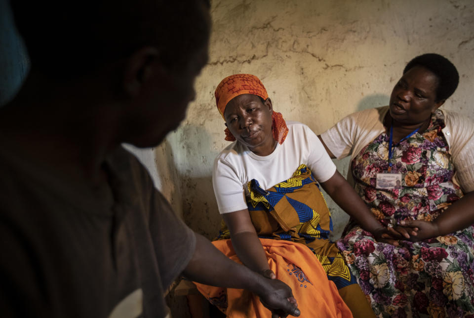 In this photo taken Tuesday, Nov. 5, 2019, palliative care nurse Madeleine Mukantagara, 56, right, comforts and prays with Faina Nyirabaguiza, 52, center, who has cervical cancer, accompanied by Faina's husband Felicien Musemihari, left, after giving her an increased dose of oral liquid morphine during a visit to check on her health at her home in the village of Ruesero, near Kibogora, in western Rwanda. While people in rich countries are dying from overuse of prescription painkillers, people in Rwanda and other poor countries are suffering from a lack of them, but Rwanda has come up with a solution to its pain crisis - it's morphine, which costs just pennies to produce and is delivered to households across the country by public health workers. (AP Photo/Ben Curtis)