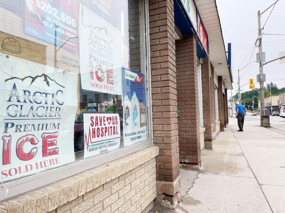 A Save Our Hospital sign is in the window of a convenience store in downtown Durham beside signs advertising ice and milk. The signs can be found throughout town on lawns and windows of other businesses.