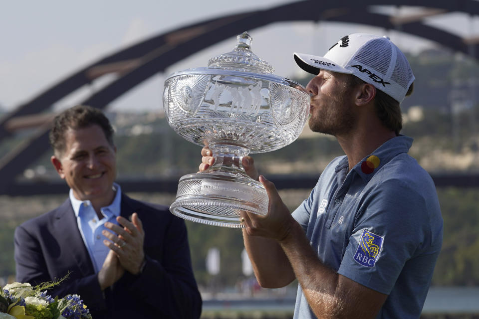 Sam Burns, right, kisses his trophy after defeating Cameron Young in the final match at the Dell Technologies Match Play Championship golf tournament in Austin, Texas, Sunday, March 26, 2023. Michael Dell, left, presented the trophy. (AP Photo/Eric Gay)