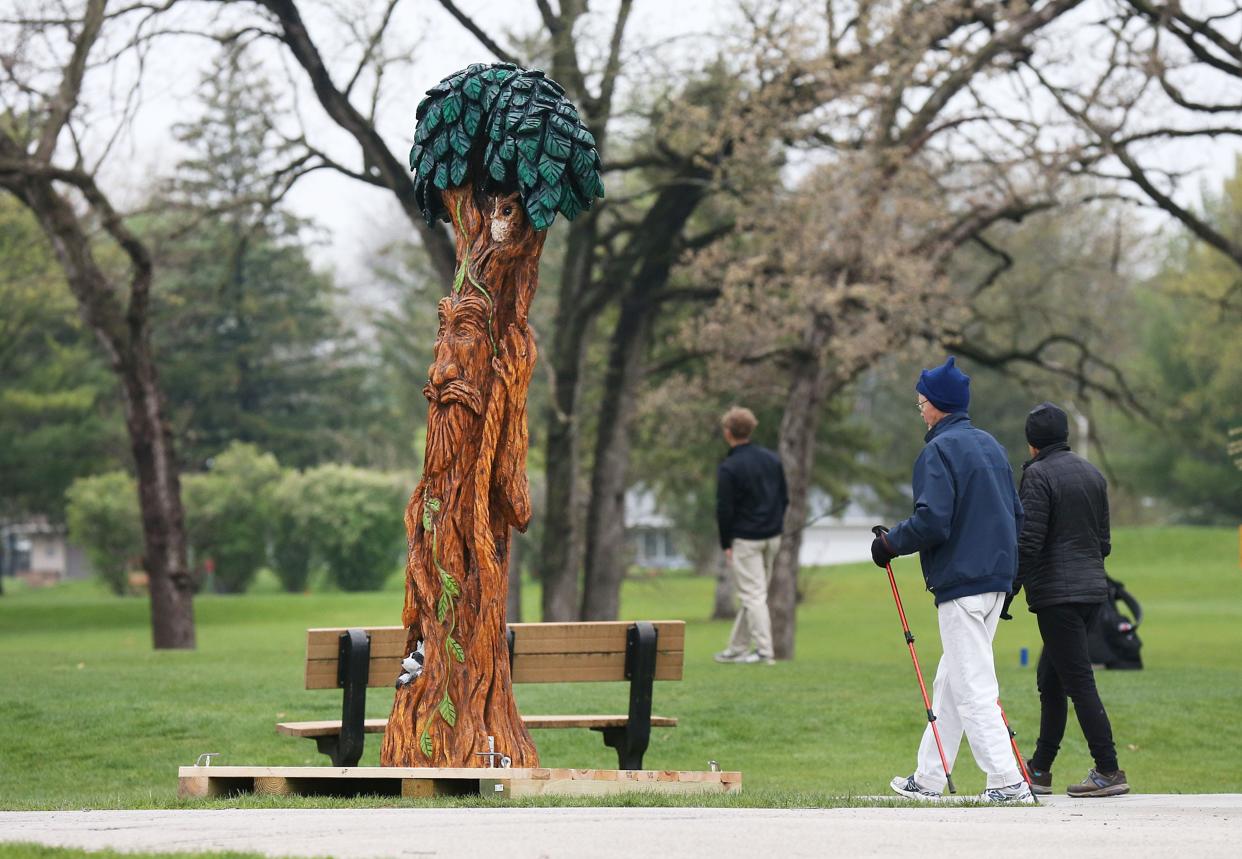 People pass by a displayed tree sculpture displays in the Arbor Day at Homewood Golf course on Friday, April 26, 2024, in Ames, Iowa.