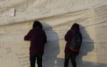 Visitors write messages on the side of a tent, wishing safe return of missing passengers aboard the sunken ferry Sewol at a port in Jindo, south of Seoul, South Korea, Tuesday, April 22, 2014. One by one, coast guard officers carried the newly arrived bodies covered in white sheets from a boat to a tent on the dock of this island, the first step in identifying a sharply rising number of corpses from the South Korean ferry that sank nearly a week ago. (AP Photo/Lee Jin-man)