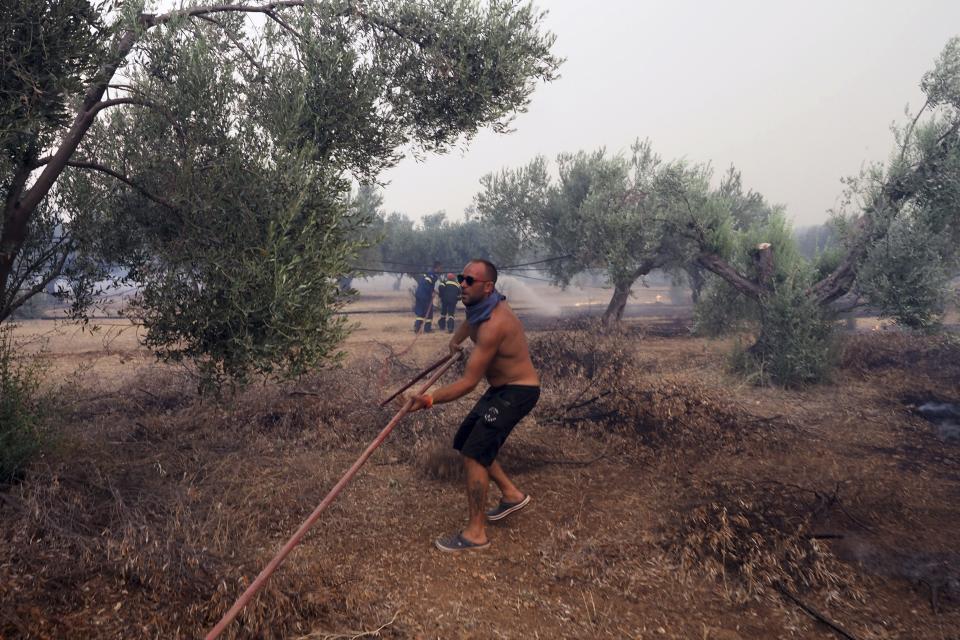 A man helps the firefighters as a wildfire burns near Vatontas village on the Aegean Sea island of Evia, Greece, Monday, Aug. 21, 2023. Major wildfires were burning in Greece and on one of Spain's Canary Islands off the African coast Monday, with hot, dry and windy conditions hampering the efforts of hundreds of firefighters battling the blazes, two of which have been burning for several days. (AP Photo/Thodoris Nikolaou)